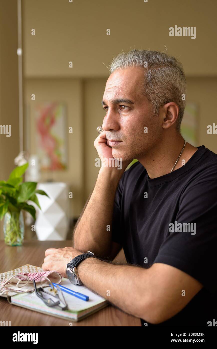 Schöner persischer Mann mit grauem Haar, der denkt und schaut Das Fenster in der Bibliothek Stockfoto