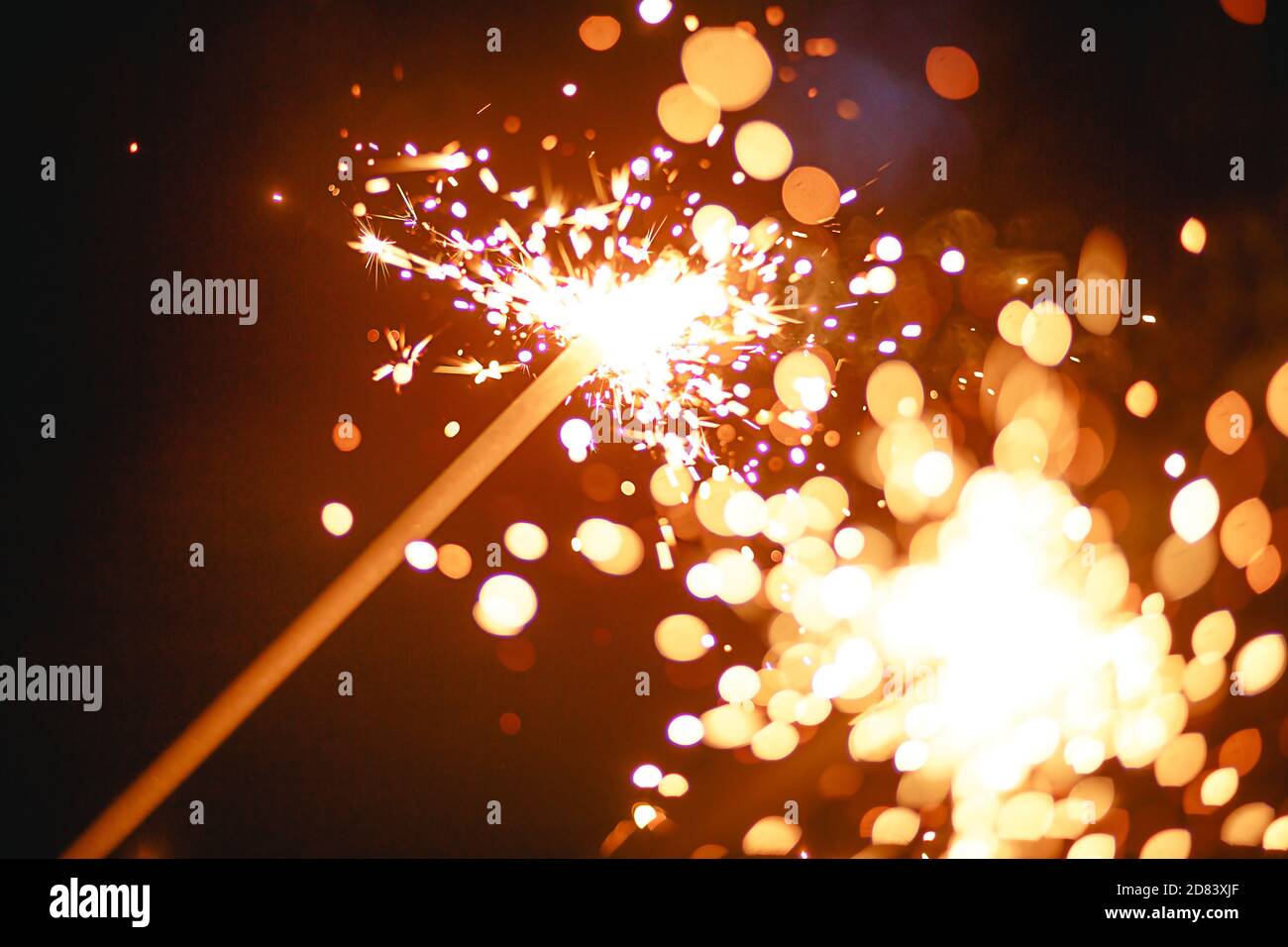 Funken und Licht von Wunderkerzen im Dunkeln mit hellem Gelb und Orange Bokeh und Rauch. Festliche Feuer Textur, Hintergrund für Neujahr und Weihnachten Stockfoto