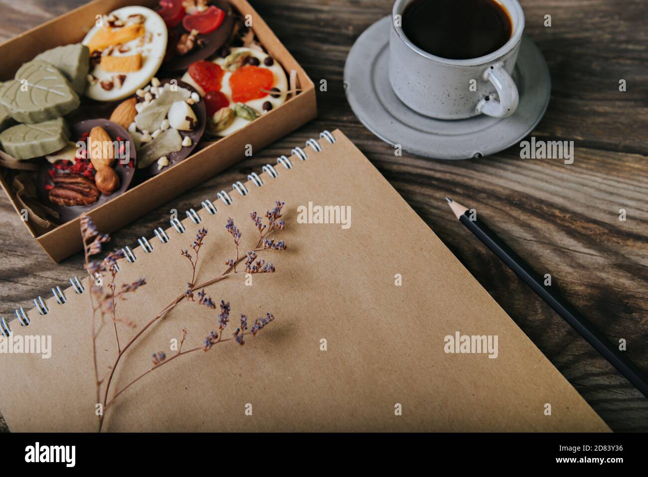 Pralinen mit getrockneten Früchten in einer Schachtel und Bastelpapier-Notizbuch in der Nähe der Tasse Kaffee. Ort für Ihren Text. Stockfoto