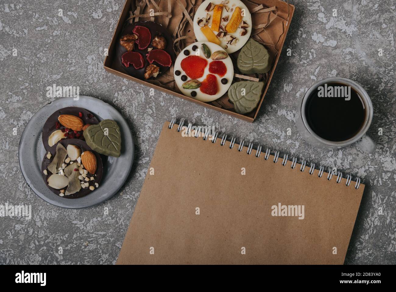 Pralinen mit getrockneten Früchten in einer Schachtel und Bastelpapier-Notizbuch in der Nähe der Tasse Kaffee. Ort für Ihren Text. Stockfoto