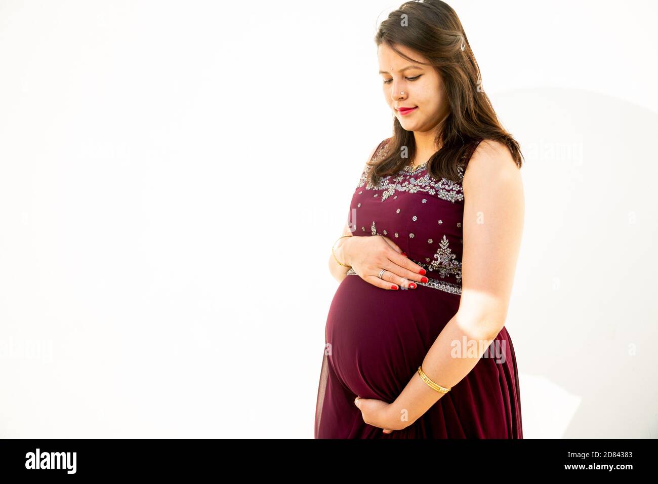 Junge asiatische indische schwangere Frau Blick auf Bauch stehen vor weißem Hintergrund im Freien Studio erschossen, glücklich Frau erwartet Baby, Mutterschaft und Stockfoto