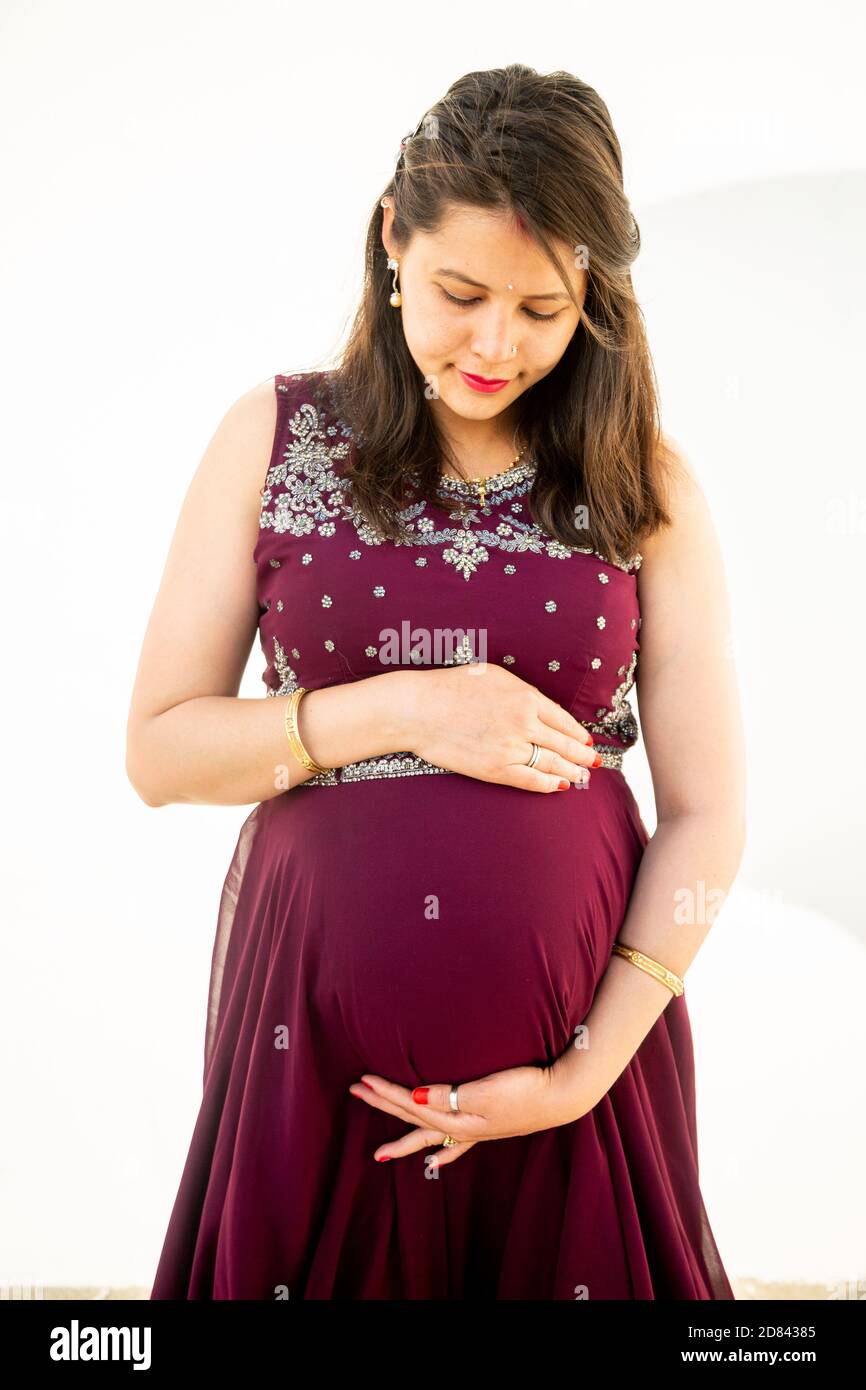 Junge asiatische indische schwangere Frau Blick auf Bauch stehen vor weißem Hintergrund im Freien Studio erschossen, glücklich Frau erwartet Baby, Mutterschaft und Stockfoto