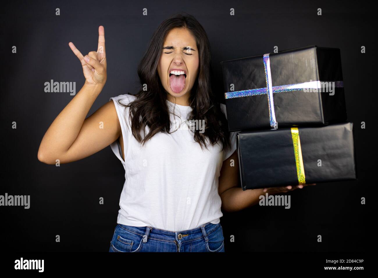 Junge schöne Frau hält Geschenke über isolierten schwarzen Hintergrund schreien Mit verrückten Ausdruck tun Rock-Symbol mit Händen nach oben Stockfoto