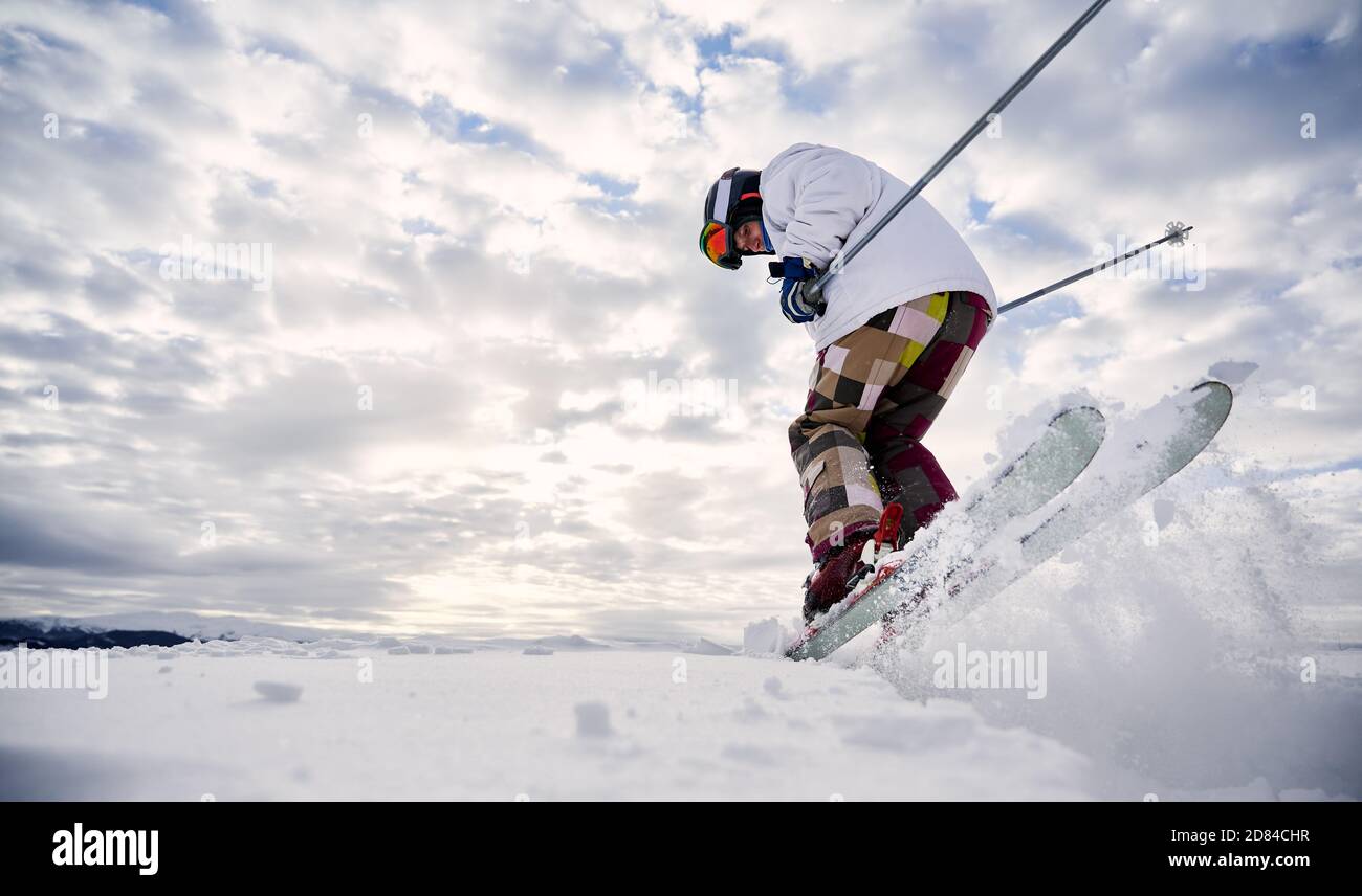 Low-Angle-Ansicht Momentaufnahme der Skier Beine tragen bunte Skihose machen einen Sprung auf weißen schneebedeckten Oberfläche gegen schönen bewölkten Himmel. Speicherplatz kopieren. Konzept der Wintersport-Aktivitäten. Stockfoto