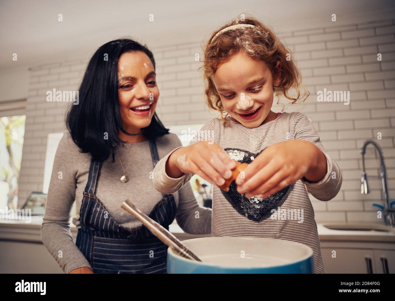 Lächelnde Mutter hilft Tochter brechen Ei für die Vorbereitung Teig in Küche Stockfoto