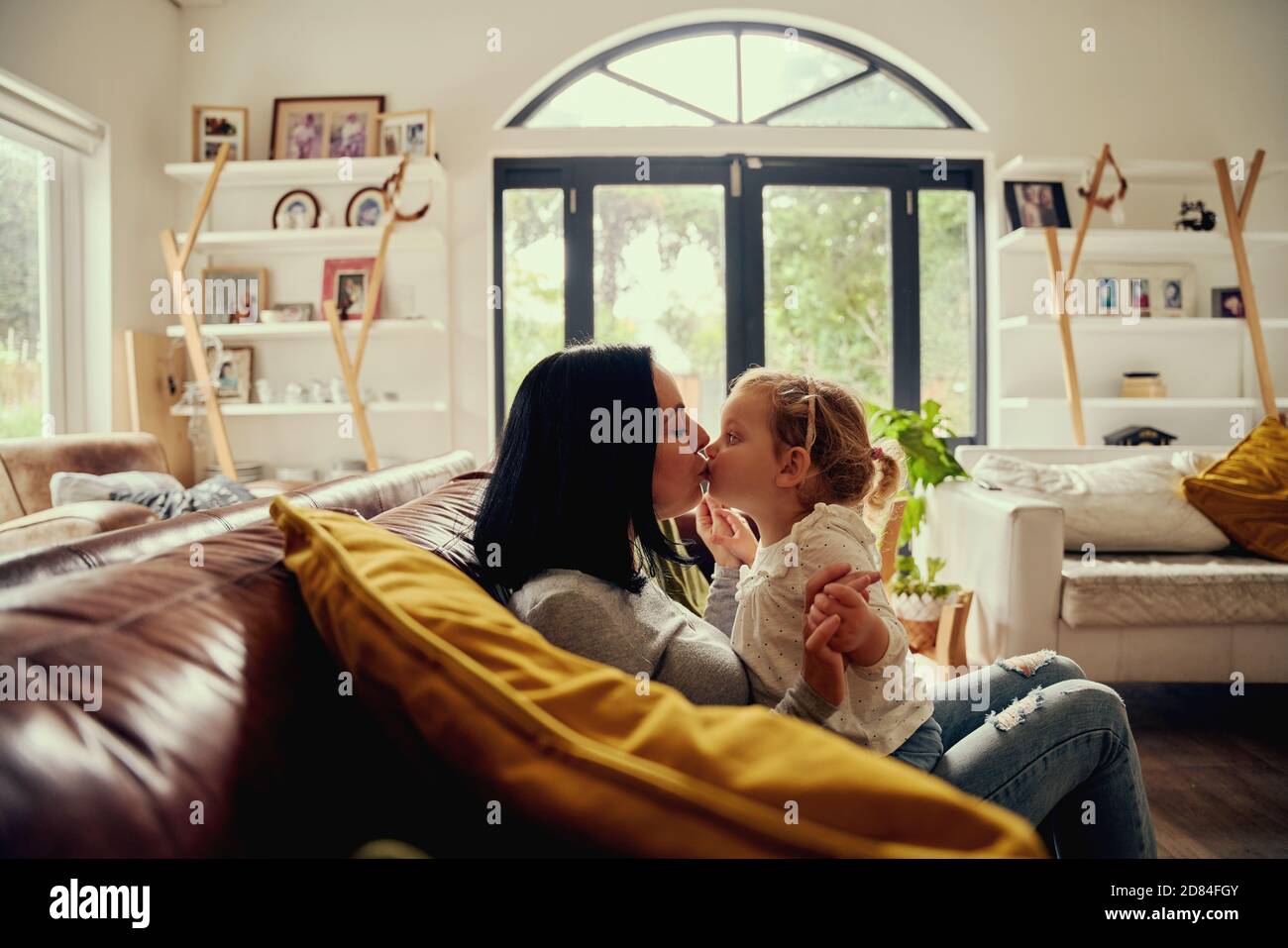Verspielte junge Frau küssen Kleinkind Mädchen, während auf dem Sofa sitzen Zu Hause Stockfoto