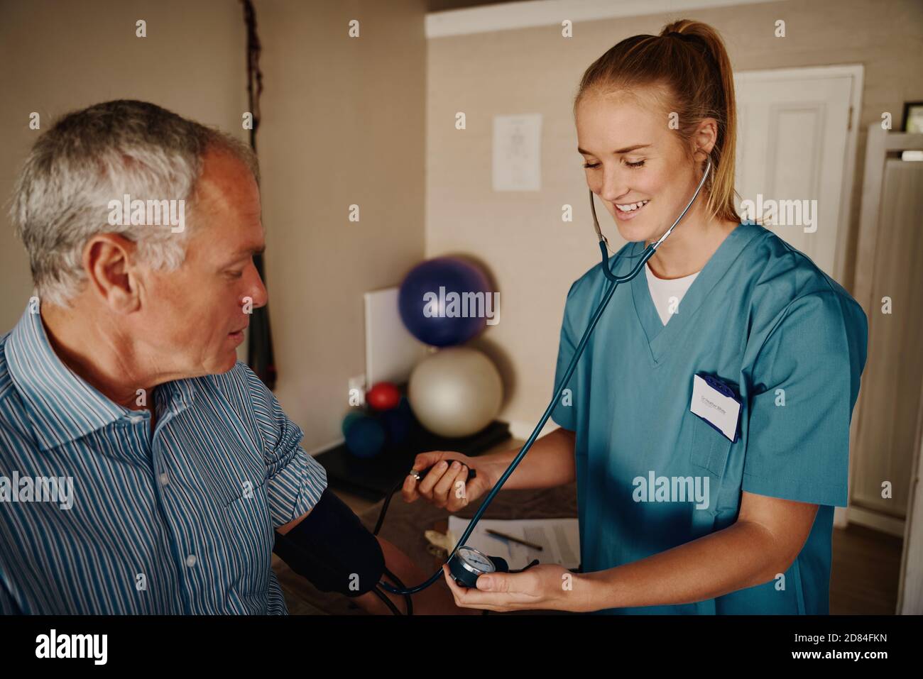 Lächelnd junge Frau Arzt Überprüfung Senior Patient Blutdruck mit Instrument und Stethoskop in der Klinik Stockfoto