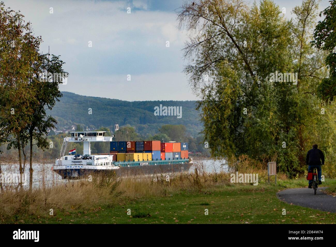 DEUTSCHLAND, Bonn, Nordrhein-Westfalen, Frachtschiff mit Containern auf dem Rhein, der von einem beliebten Radweg für h gesäumt wird Stockfoto