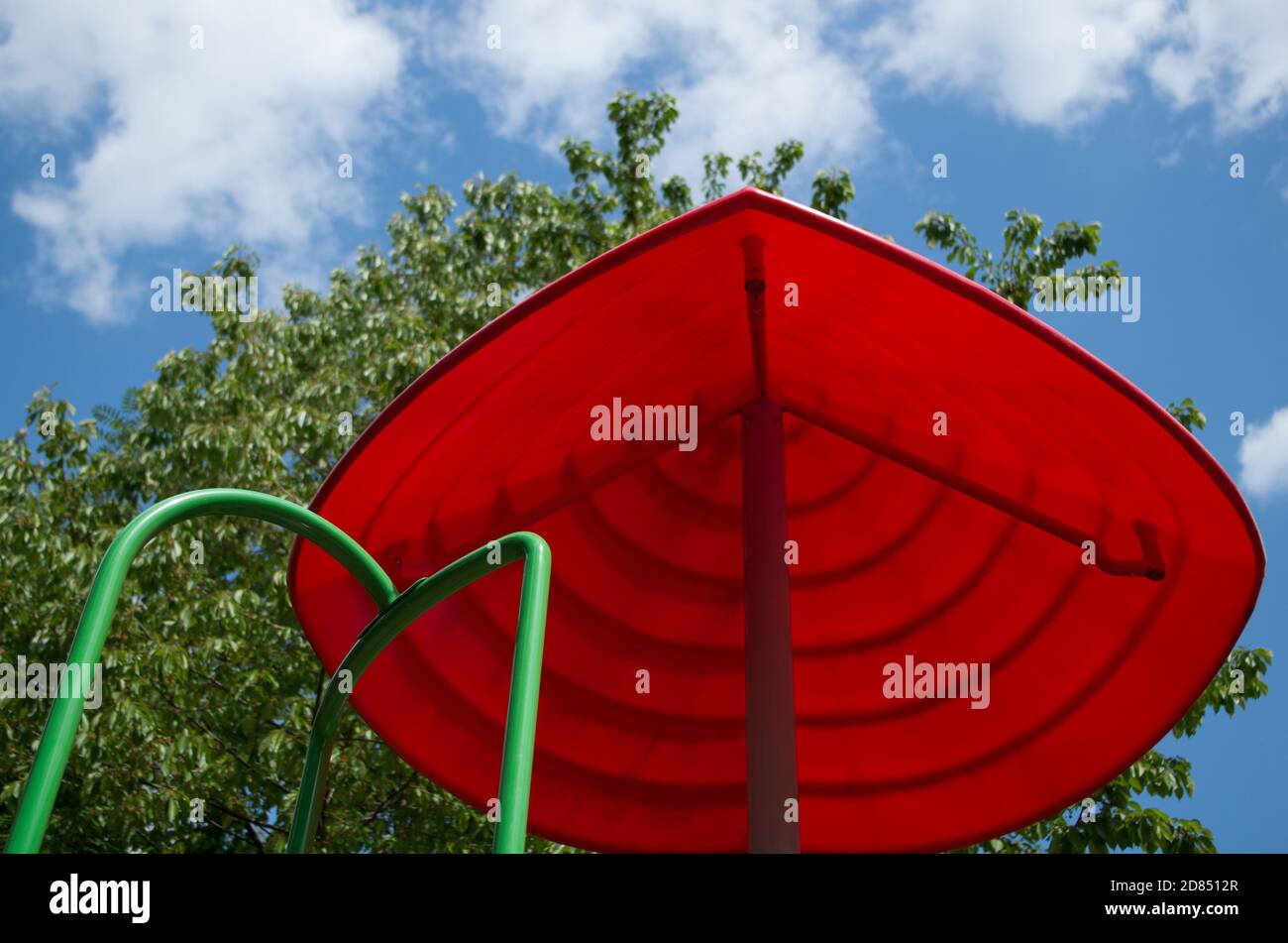Rote Pyramide oder Schirm geformt Visier mit grünen Handlauf führenden Ihm auf dem Kinderspielplatz auf dem Hintergrund des Baumes Laub und wolkig blauer Himmel Stockfoto