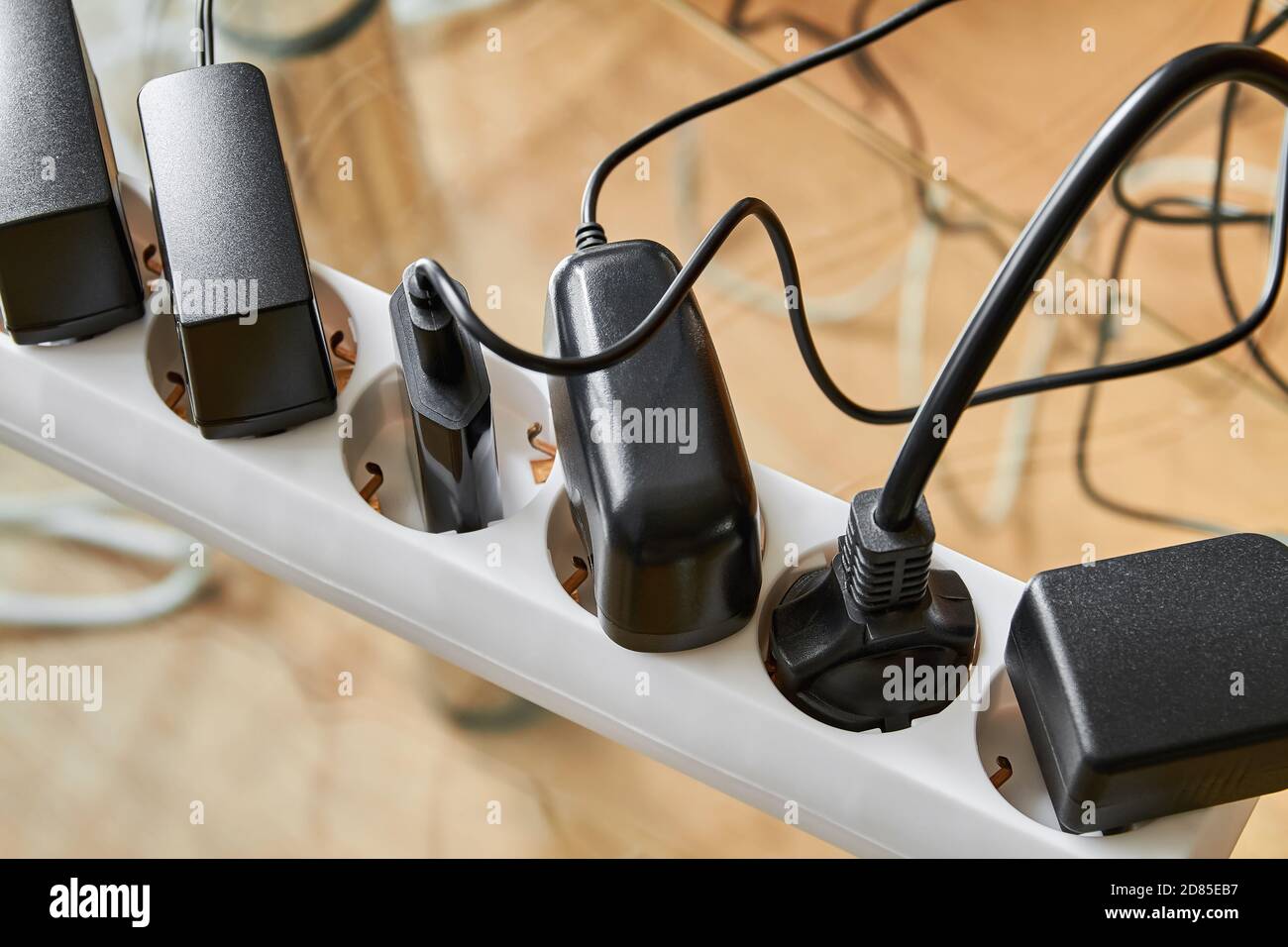 Die Steckerleiste ist überlastet, da mehrere Netzkabel eingesteckt sind. Viele Stecker sind an die Stromschiene angeschlossen Stockfoto