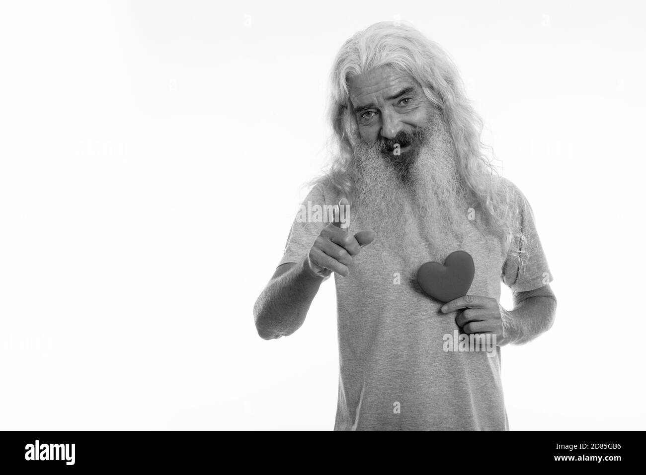 Studioaufnahme eines glücklichen älteren bärtigen Mannes, der lächelte und zeigte Vor der Kamera, während das Herz für den Valentinstag bereit hält Stockfoto