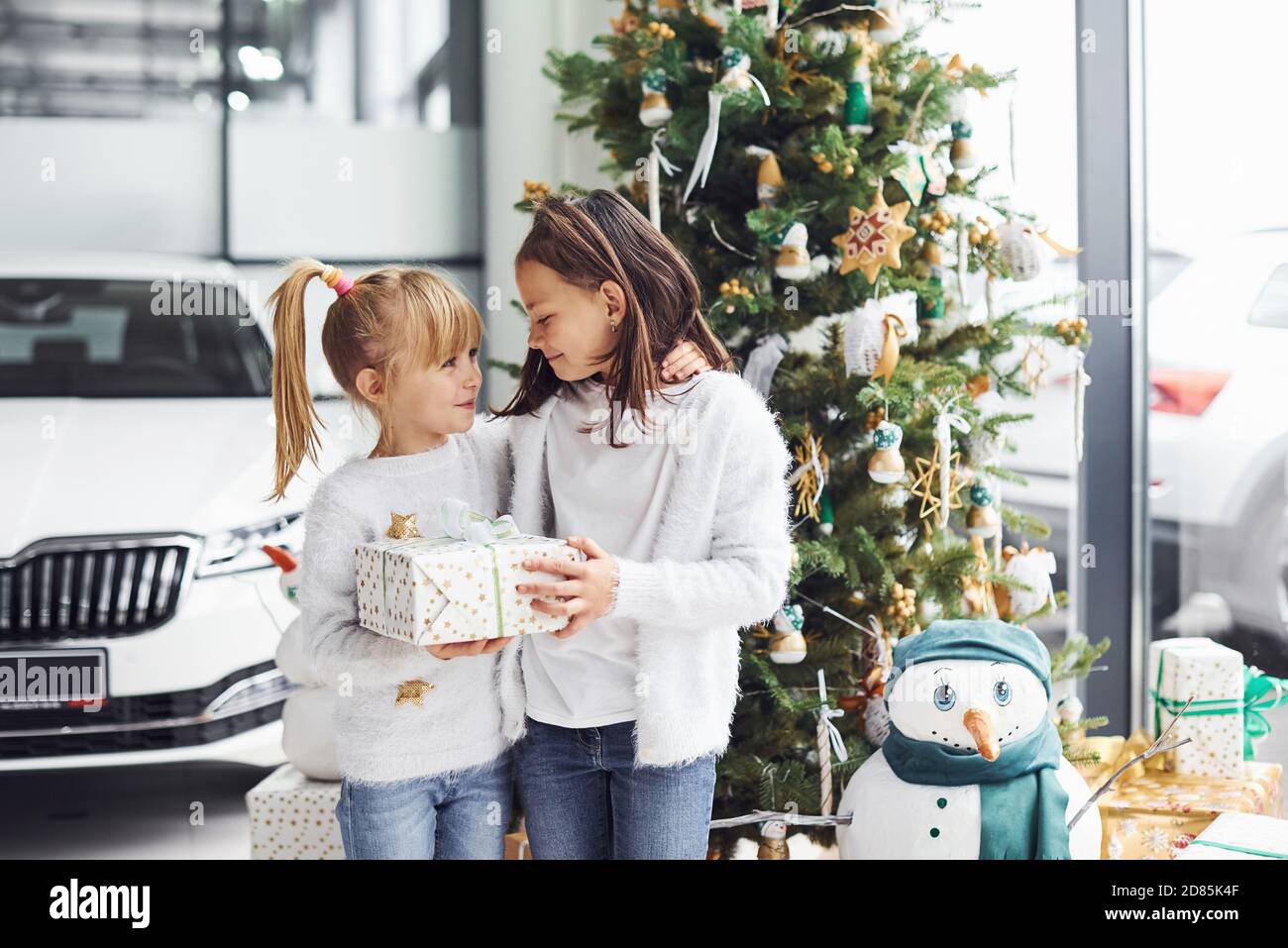 Zwei niedliche kleine Mädchen stehen in der Nähe von Auto und weihnachtsbaum Mit Geschenkbox für das neue Jahr Stockfoto