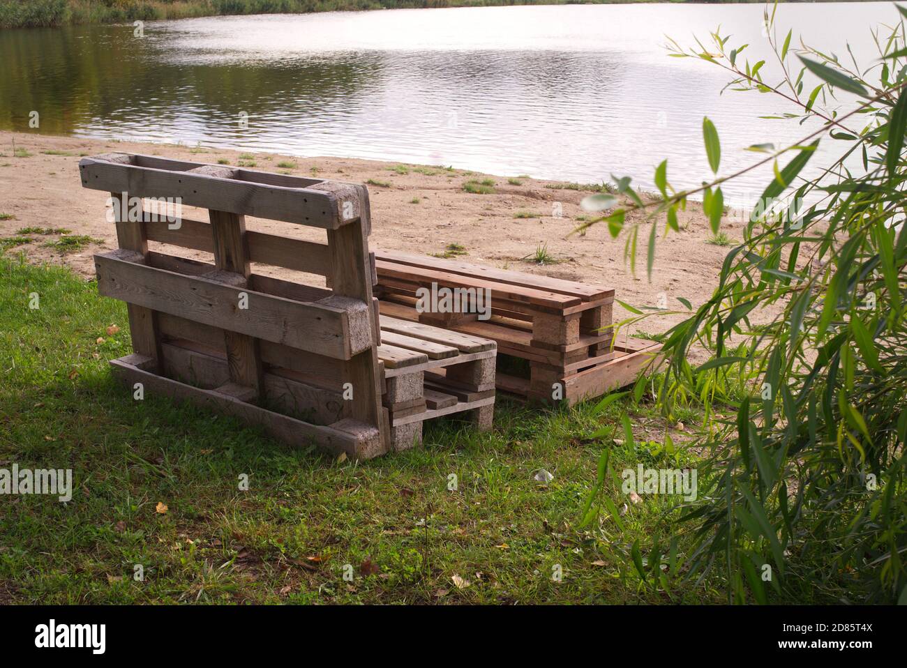 Gartenmöbel aus Holzpaletten am Ufer Ein ruhiger See, umgeben von Bäumen und viel Grün Sommersonne Stockfoto