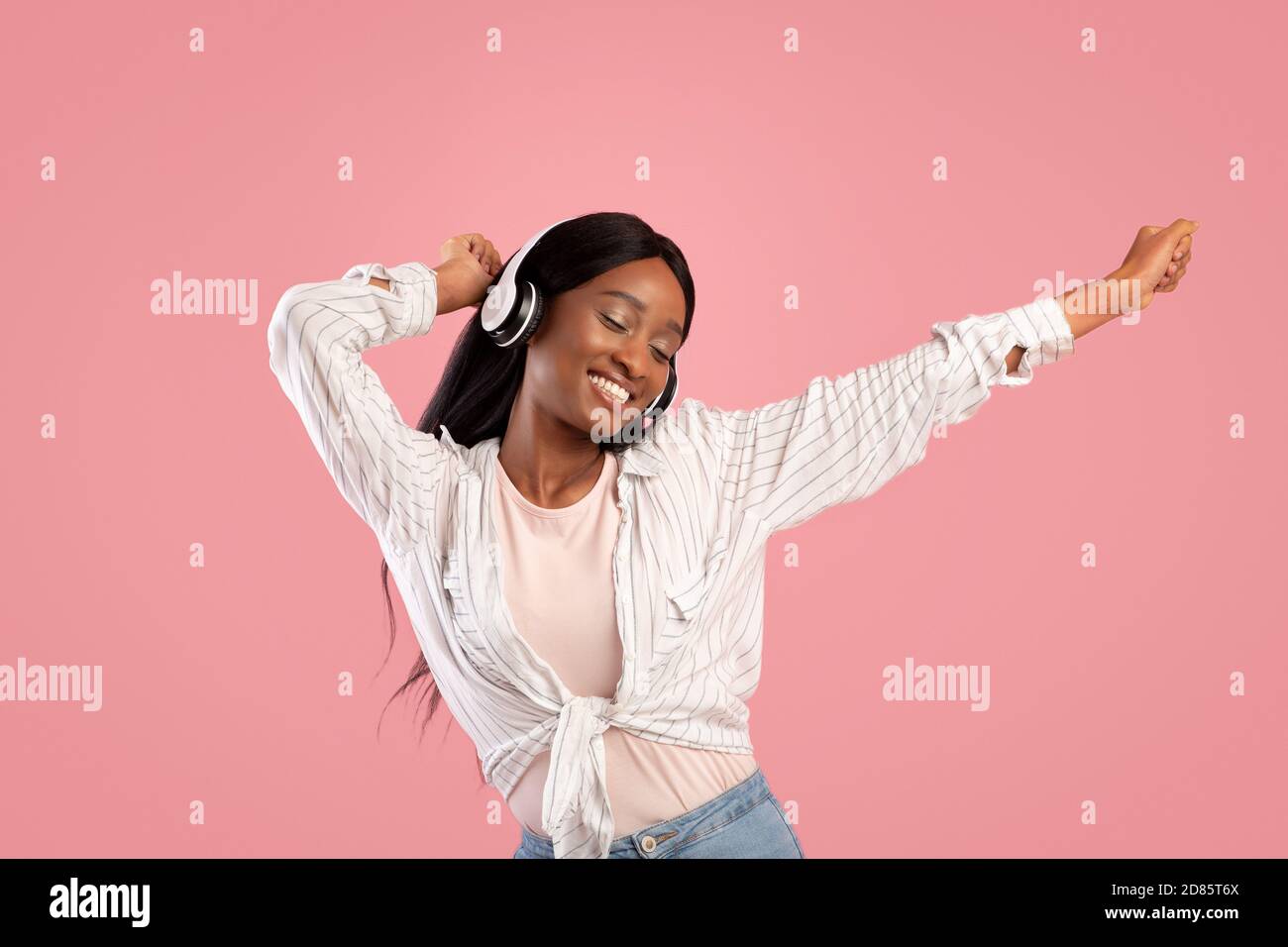 Glückliche schwarze Frau im Headset tanzen zu schöner Musik auf Rosa Studio Hintergrund Stockfoto