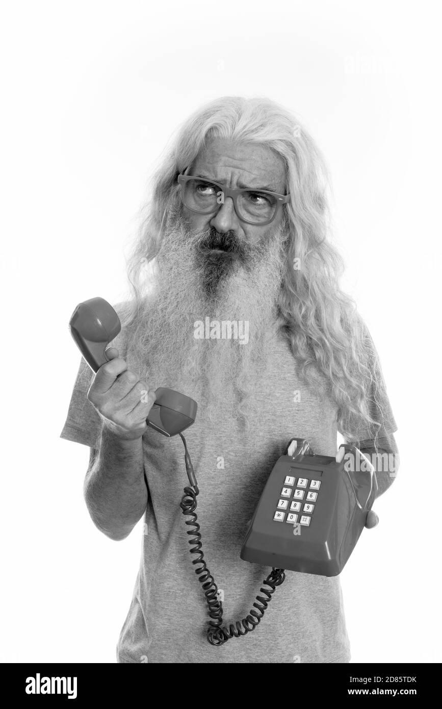 Studio shot der älteren bärtigen Mann mit alten Telefon beim Denken und Suchen Stockfoto