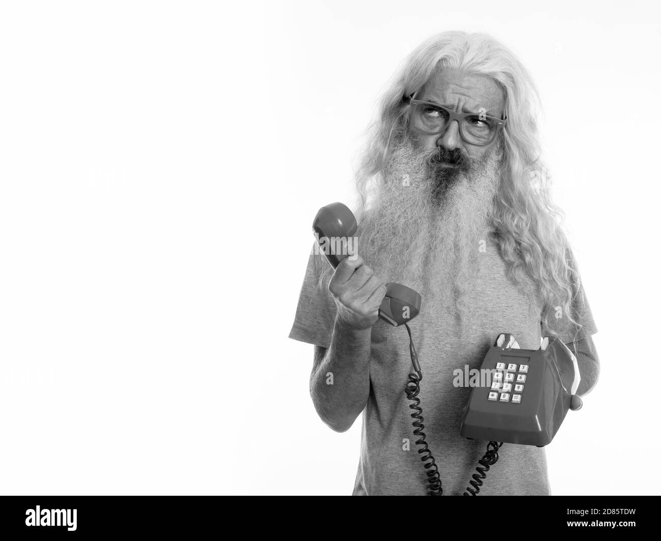 Studio shot der älteren bärtigen Mann mit alten Telefon beim Denken und Suchen Stockfoto
