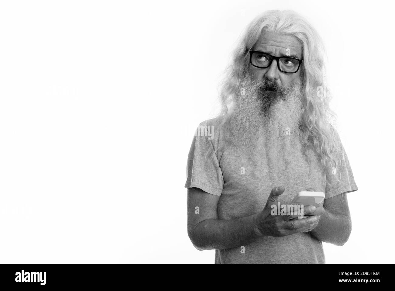 Studio shot der älteren bärtigen Mann denken, während Sie Handy Stockfoto