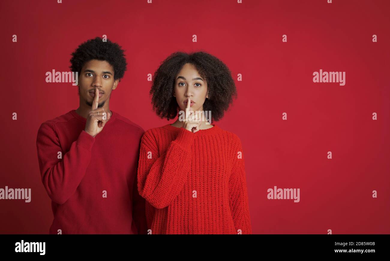 Ruhige afroamerikanische junge weibliche und männliche in Pullover machen Stille Zeichen, halten Vorderfinger auf den Lippen Stockfoto
