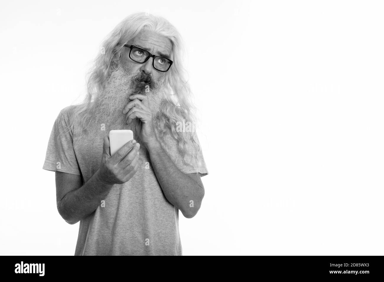 Studio shot der älteren bärtigen Mann denken, während Sie Handy Stockfoto
