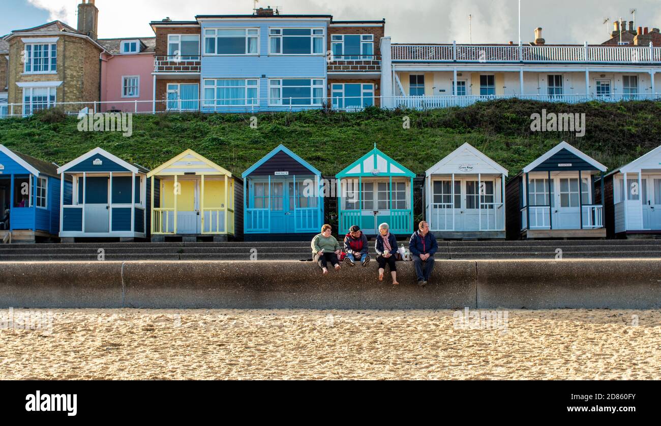 Vier Leute sitzen auf der Promenade mit Strandhütten dahinter, Southwold, Suffolk, Großbritannien Stockfoto