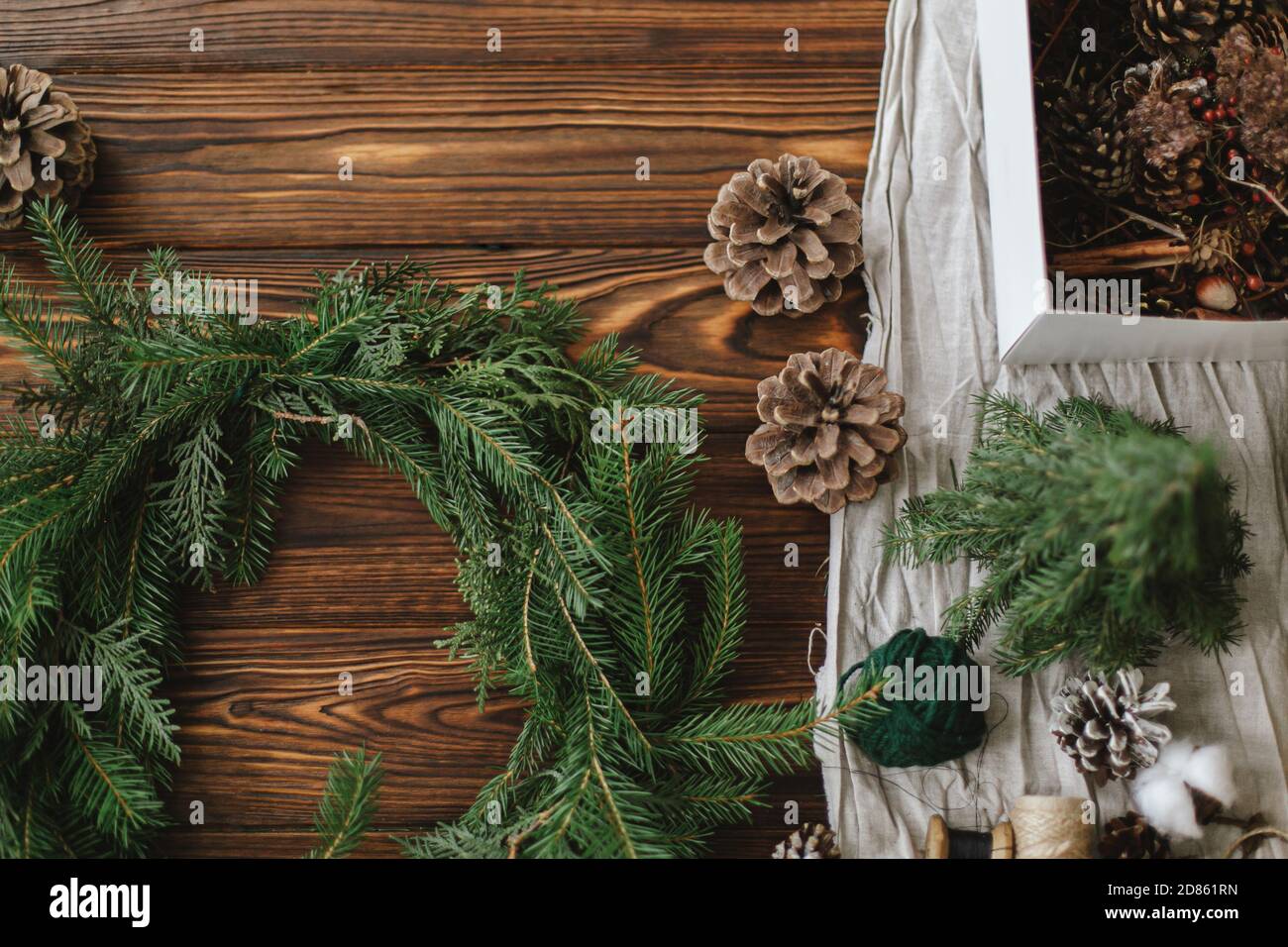 Rustikalen weihnachtskranz auf Holztisch machen. Weihnachtskranz mit Beeren, grünen Tannenzweigen, Tannenzapfen und natürlichen festlichen Dekorationen auf Rost Stockfoto