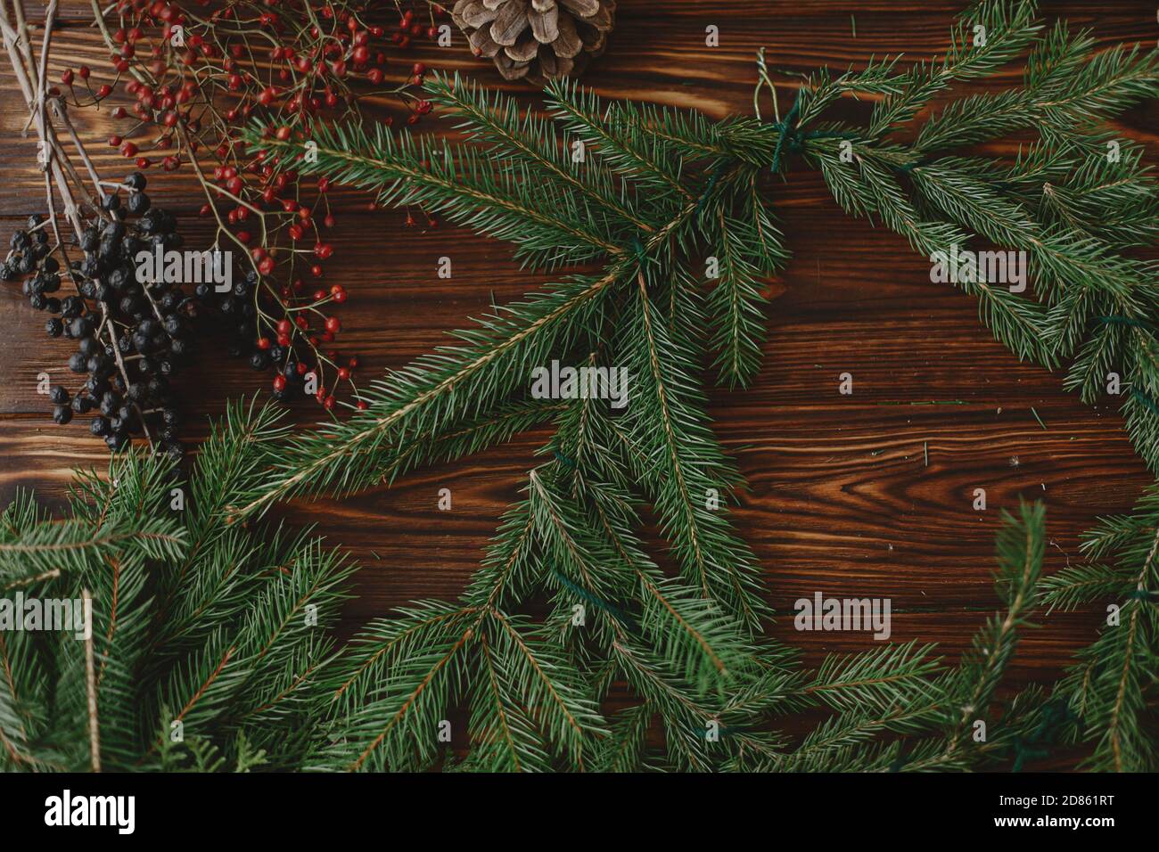 Rustikalen weihnachtskranz auf Holztisch machen. Weihnachtskranz mit roten Beeren, grünen Tannenzweigen, Tannenzapfen und natürlichen festlichen Dekorationen auf r Stockfoto