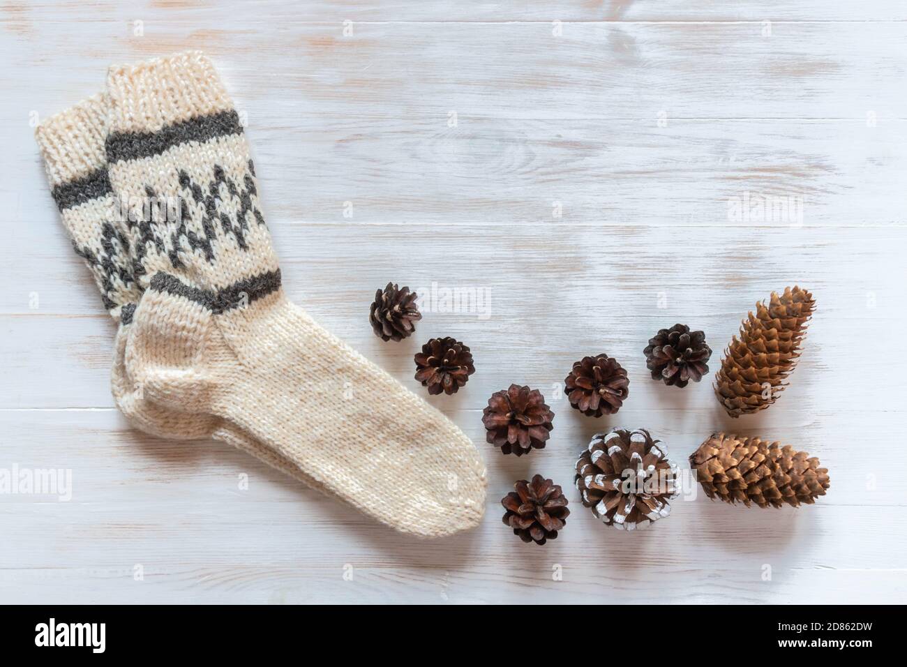 Warme Wollsocken für die kalte Jahreszeit und Tannenzapfen auf Vintage Holz Hintergrund. Wollsocken für den Winter auf weißer Holzoberfläche mit Platz für Text Stockfoto