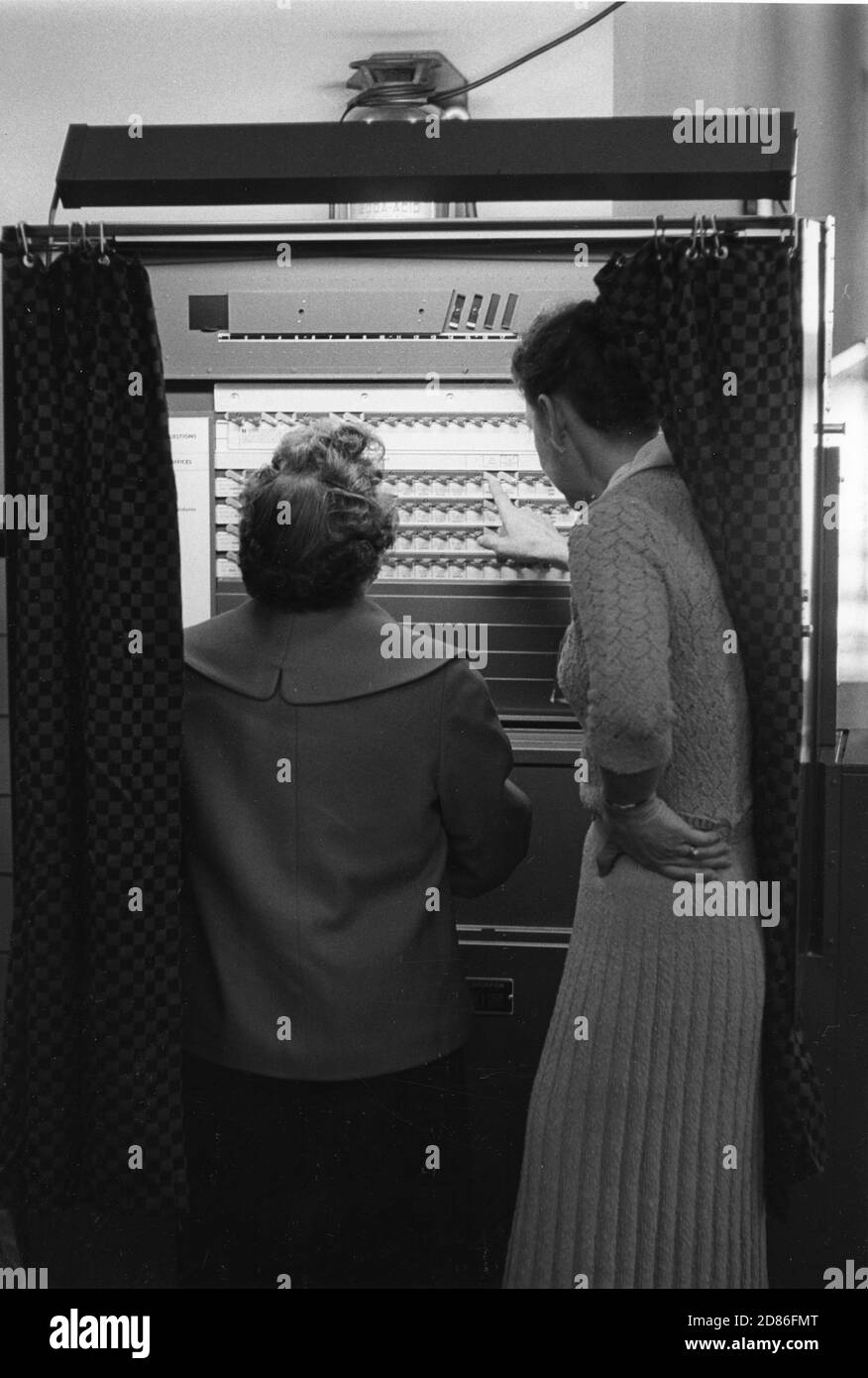 Die Wähler in dieser Gemeinschaft benutzen zum ersten Mal Wahlmaschinen. Ein Wahlbeamter erklärt einem Wähler das Wahlverfahren für die Kandidaten ihrer Wahl, Falls Church, VA, 11/8/1960. (Foto von Edwin Huffman/United States Information Agency/RBM Vintage Images) Stockfoto