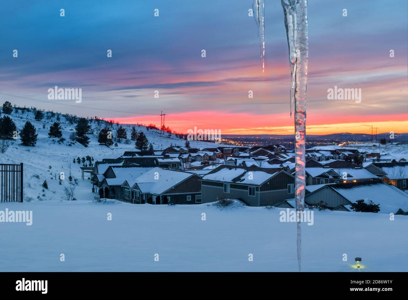 Ein farbenfroher, kälter Winterhimmel und Sonnenuntergang über Spokane Washington von einem Haus auf einem Hügel mit Schnee und Eiszapfen im Vordergrund gesehen. Stockfoto
