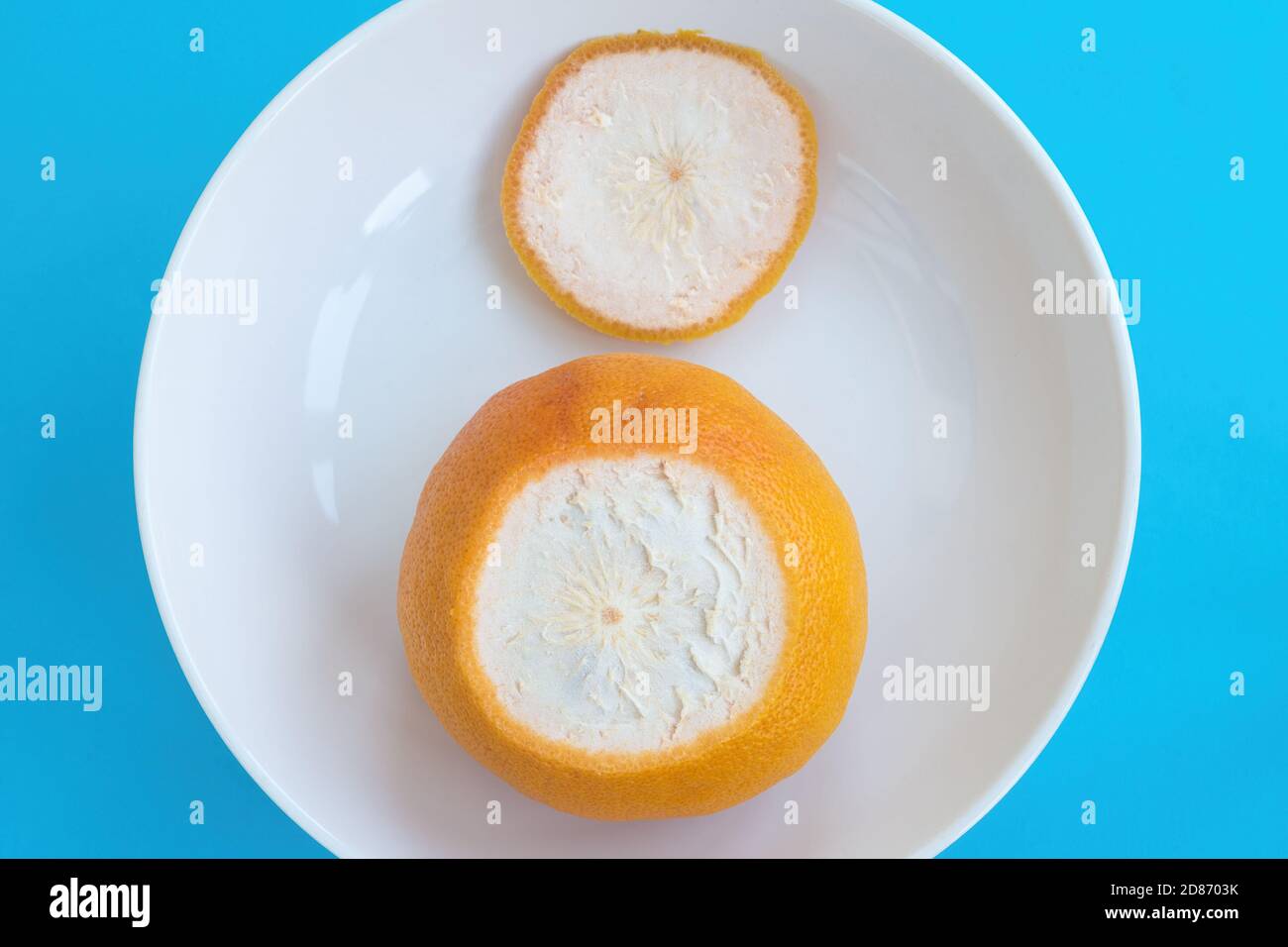 Orange Grapefruit mit abgeschnittenem oberen Ende auf weißem Teller auf blauem Hintergrund. Draufsicht, Diät-Konzept Stockfoto