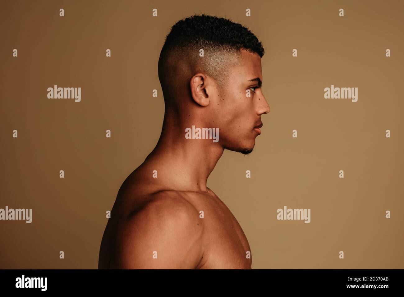 Seitenansicht eines afroamerikanischen Mannes auf braunem Hintergrund. Porträt eines gerafften muskulösen Mannes mit kurzen Haaren. Stockfoto