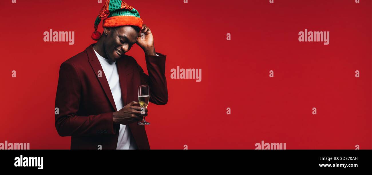 Junger Mann, der eine Partei hat steht auf roten Hintergrund mit einem Glas Champagner. African American man geniesst bei Party mit Getränken. Stockfoto