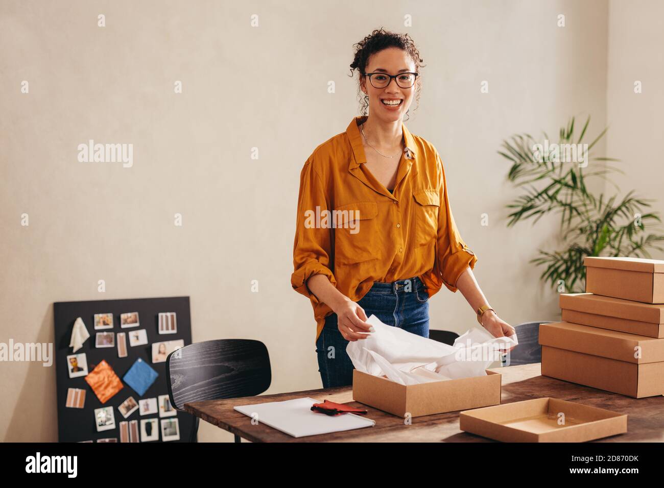 Junge Frau, die Kamera anschaut und lächelt am Drop-Shipping-Büro zu Hause. Lächelnd Online-Shop Geschäft Eigentümer Verpackung Paketboxen für Deliv Stockfoto
