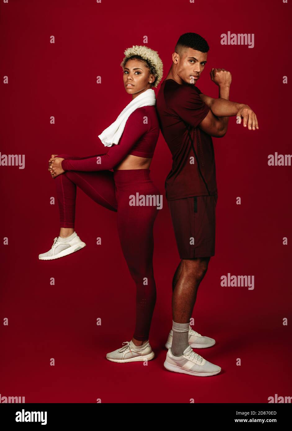 afroamerikanisches Sportpaar, das gemeinsam Fitness-Übungen macht. Fitnesspaar steht mit Rücken gegeneinander auf kastanienbraunem Hintergrund. Stockfoto