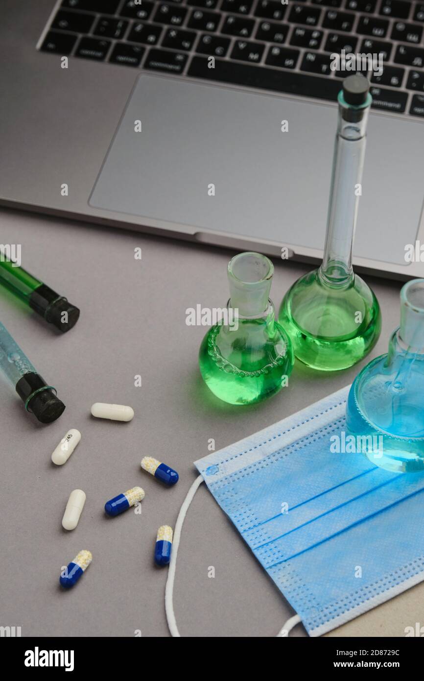 Laborflasche mit grüner und blauer Flüssigkeit und Tabletten. Forschung für die Virus Heilung und Laptop Stockfoto