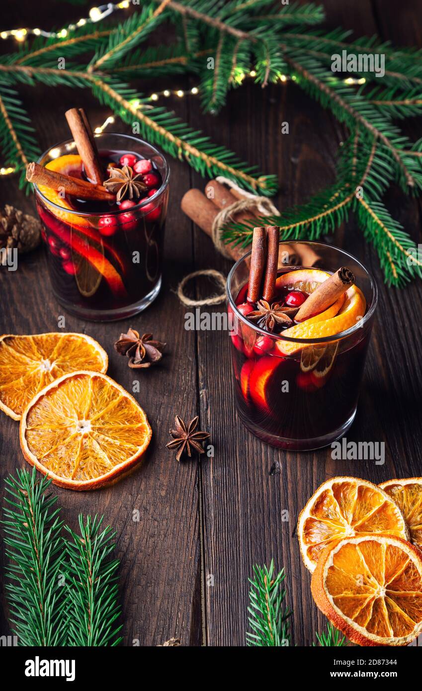 Weihnachtlicher Glühwein mit Preiselbeeren, Orange und Gewürzen auf rustikalem Holzhintergrund. Traditionelles warmes Getränk im Winter. Stockfoto