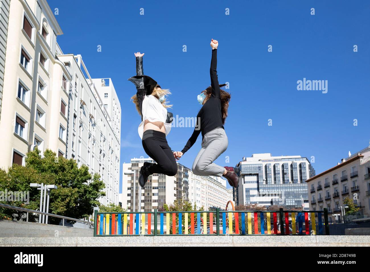 Zwei Freunde springen mit Vitalität auf der Straße. Sie tragen Gesichtsmasken. Stockfoto
