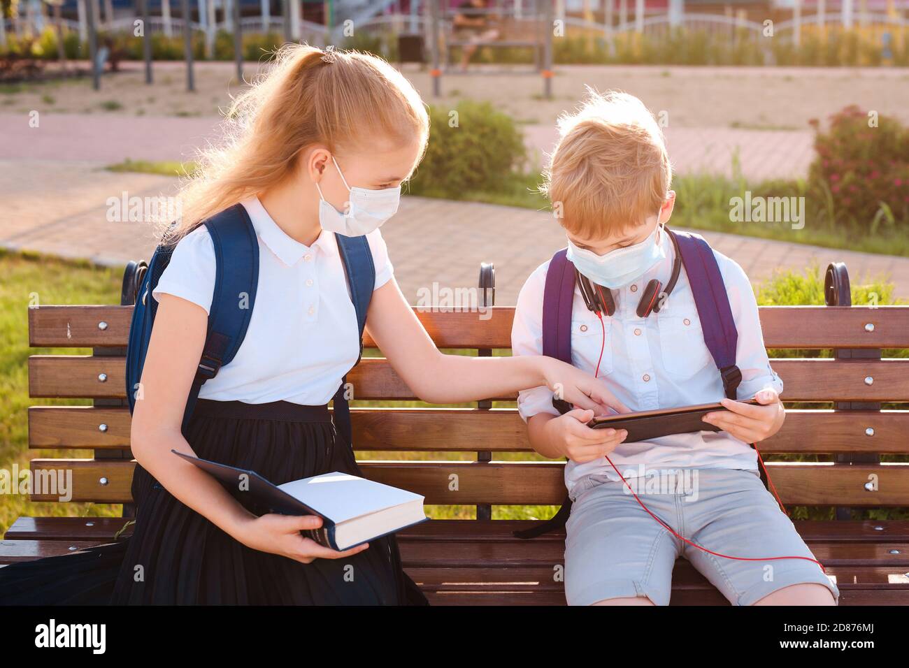 Neue Normalität: Schuljunge und Mädchen in den geschützten Masken kommunizieren und ihre Hausaufgaben auf dem Schulhof machen. Stockfoto