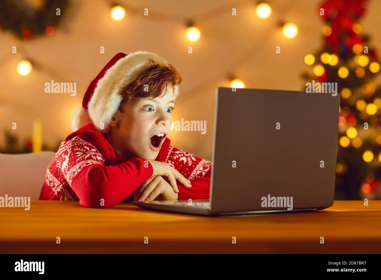 Überrascht Junge in Weihnachten festliche Kleidung und Hut Film zu sehen Online auf dem Laptop Stockfoto