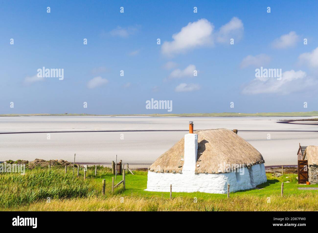 Traditionell gebaute weiße Hütte mit Strohdach, neben der türkisfarbenen Bucht, mit stürmischen bewölkten dunklen Himmel über.Insel North Uist, Schottland Stockfoto