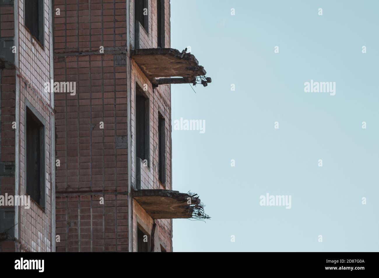 Hohe mehrstöckige verlassene sowjetische Gebäudefassade mit abgestürzten Balkonen Silhouette am Himmel. Verwittertes Haus, unvollendete Stadt der Atomwissenschaftler in Stockfoto