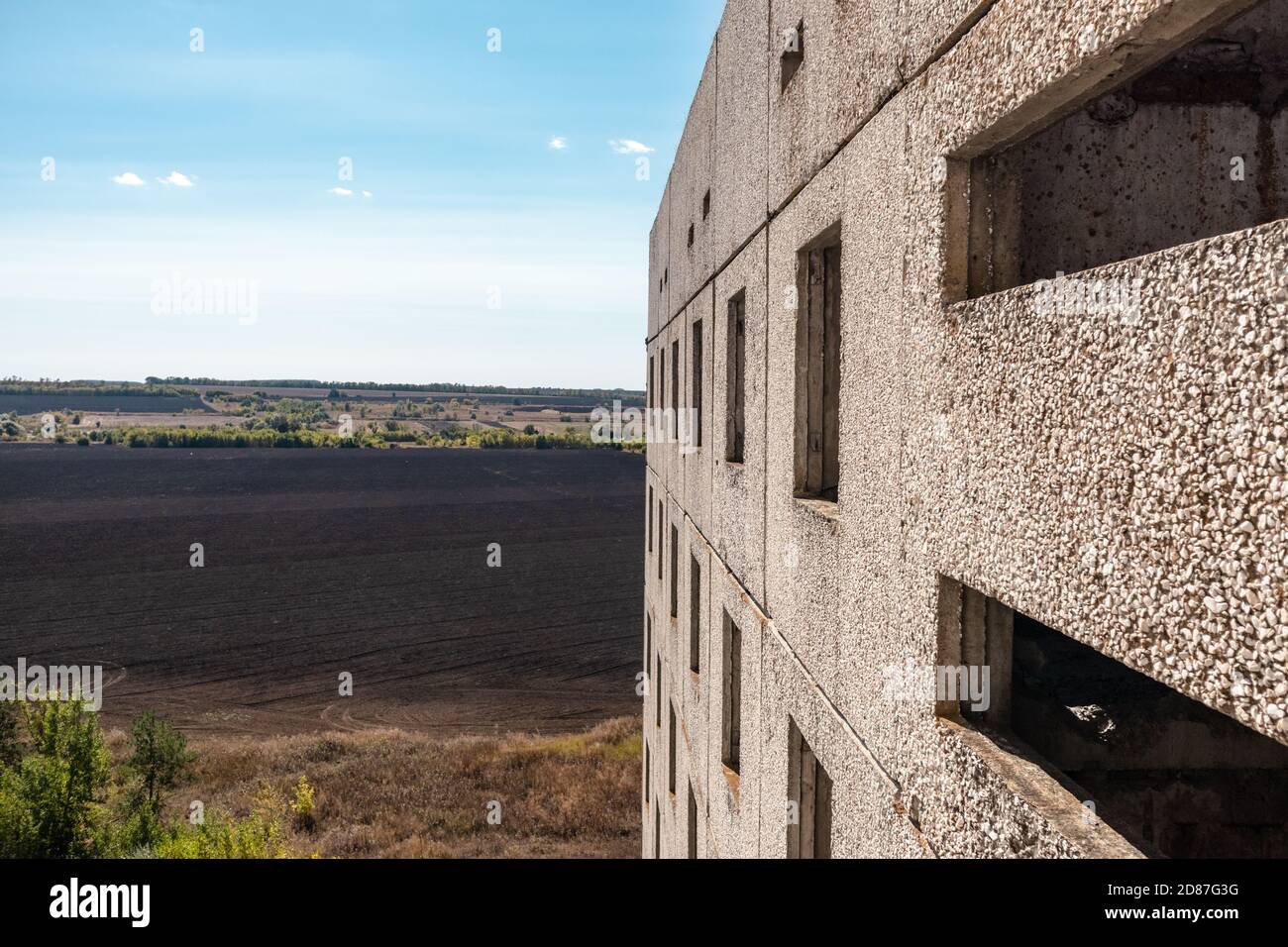 Blick aus dem Fenster des hohen mehrstöckigen verlassenen sowjetischen Gebäudes mit Fassade auf hellblaue ländliche Landschaft. Verwitterte Wohnsiedlung, unvollendete Stadt o Stockfoto