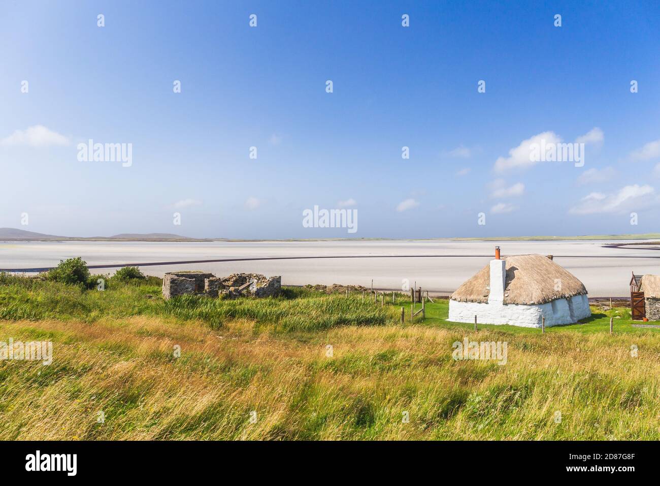 Traditionell gebaute weiße Hütte mit Strohdach, neben der türkisfarbenen Bucht, mit stürmischen bewölkten dunklen Himmel über.Insel North Uist, Schottland Stockfoto