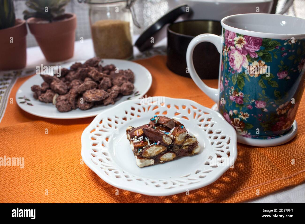 Ein Stück Nougat aus Avola-Mandeln namens "Minnulata" und eine Tasse mit Tee, vor einem Hintergrund von Pralinemandeln Stockfoto