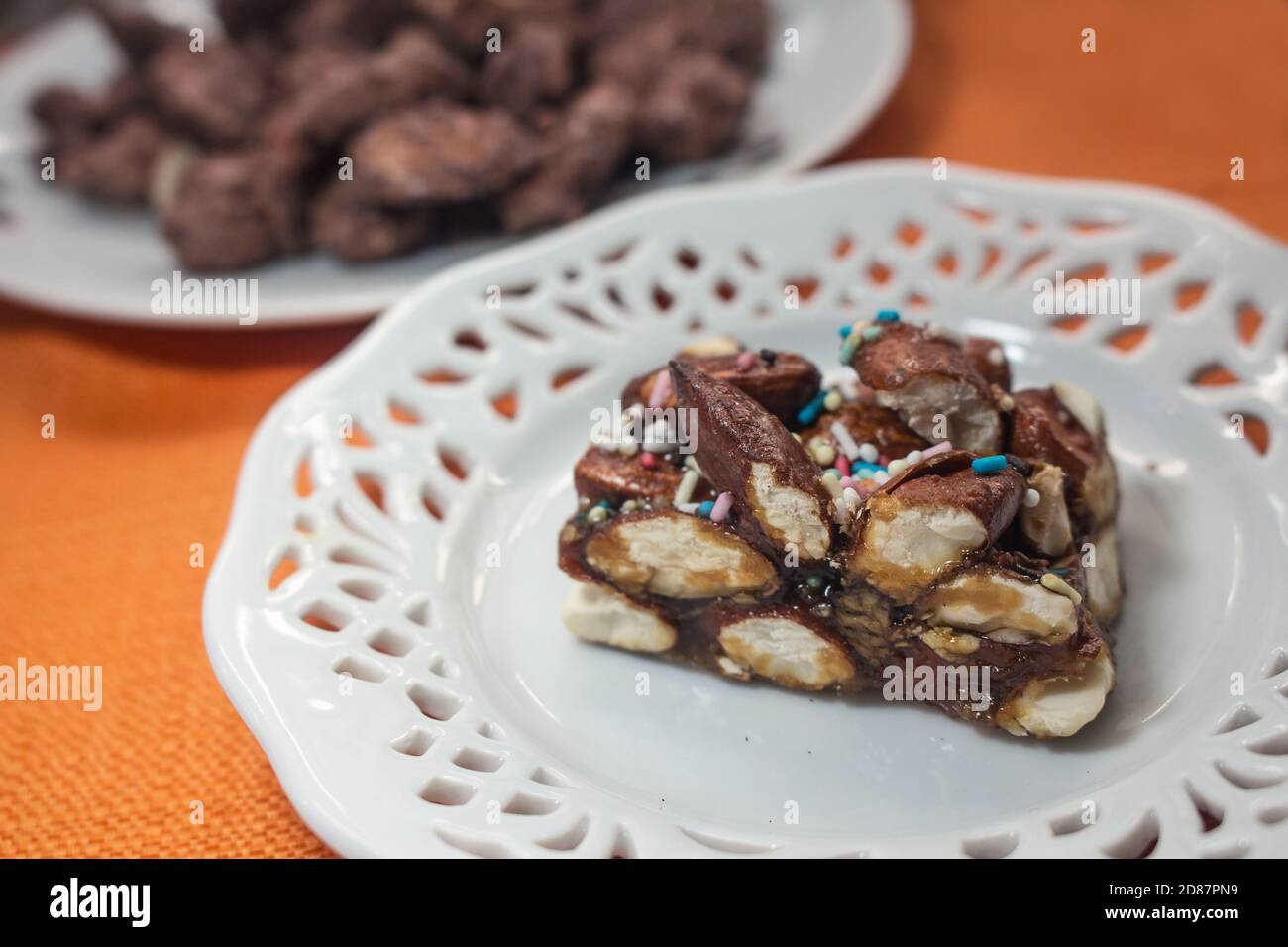 Typisches sizilianisches Dessert: Ein Stück Nougat aus Avola-Mandeln, genannt "Minnulata", vor dem Hintergrund karamellisierter Mandeln Stockfoto