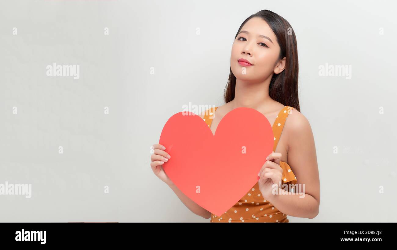 Lächelndes asiatisches Mädchen hält große rote Herzform und schaut weg Stockfoto