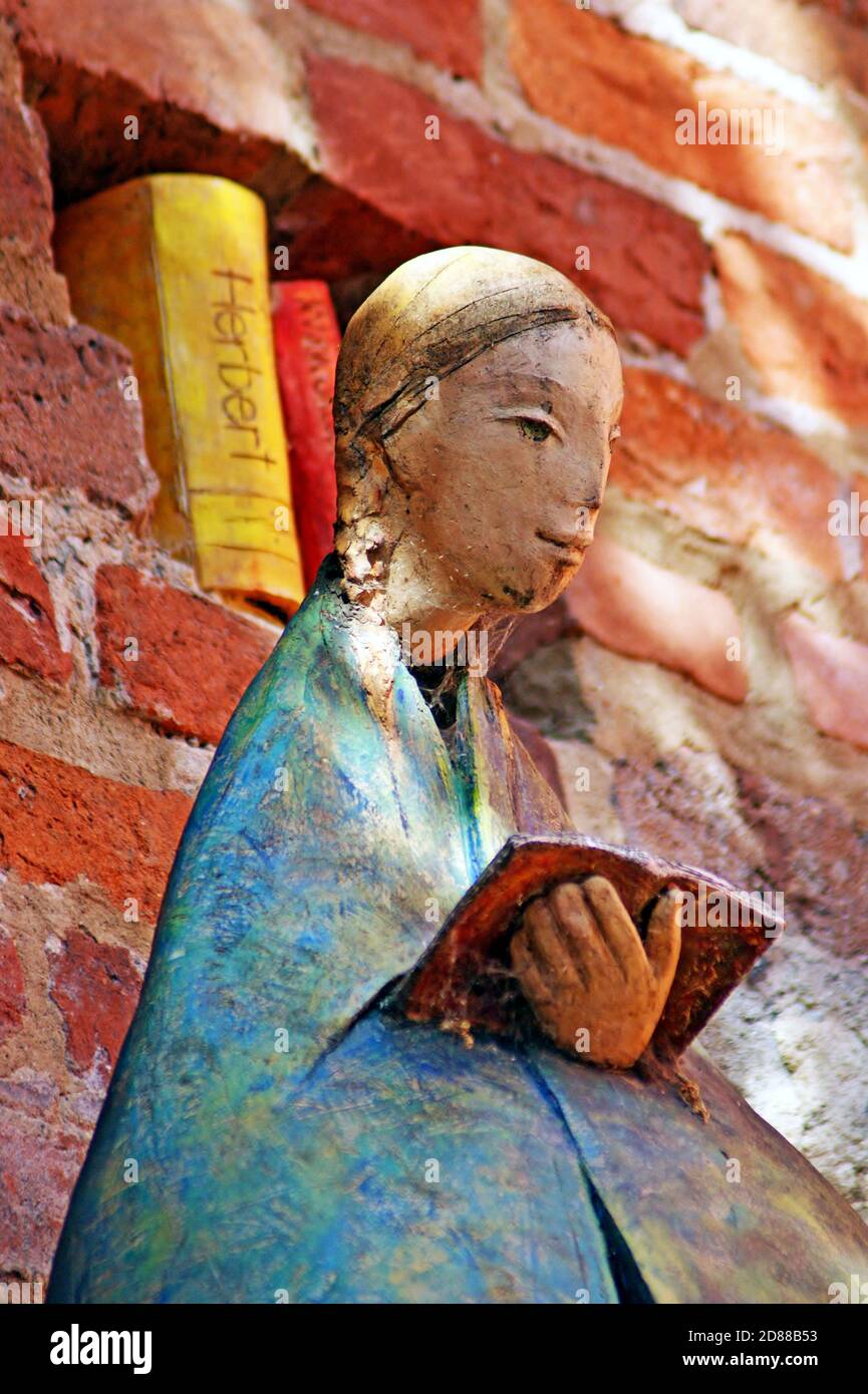Die Skulptur einer Frau, die vor den gemeißelten Büchern in einer Ziegelmauer ein Buch liest, ist eine Form der Beeinflussung der kulturellen Alphabetisierung in Torun, Polen. Stockfoto