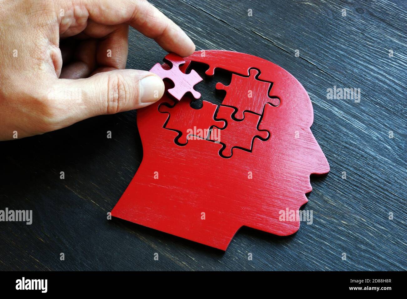 Behandlung von psychischen Erkrankungen und Gedächtnisstörungen. Die Hand legt ein Stück des Puzzles auf die Form des Kopfes. Stockfoto