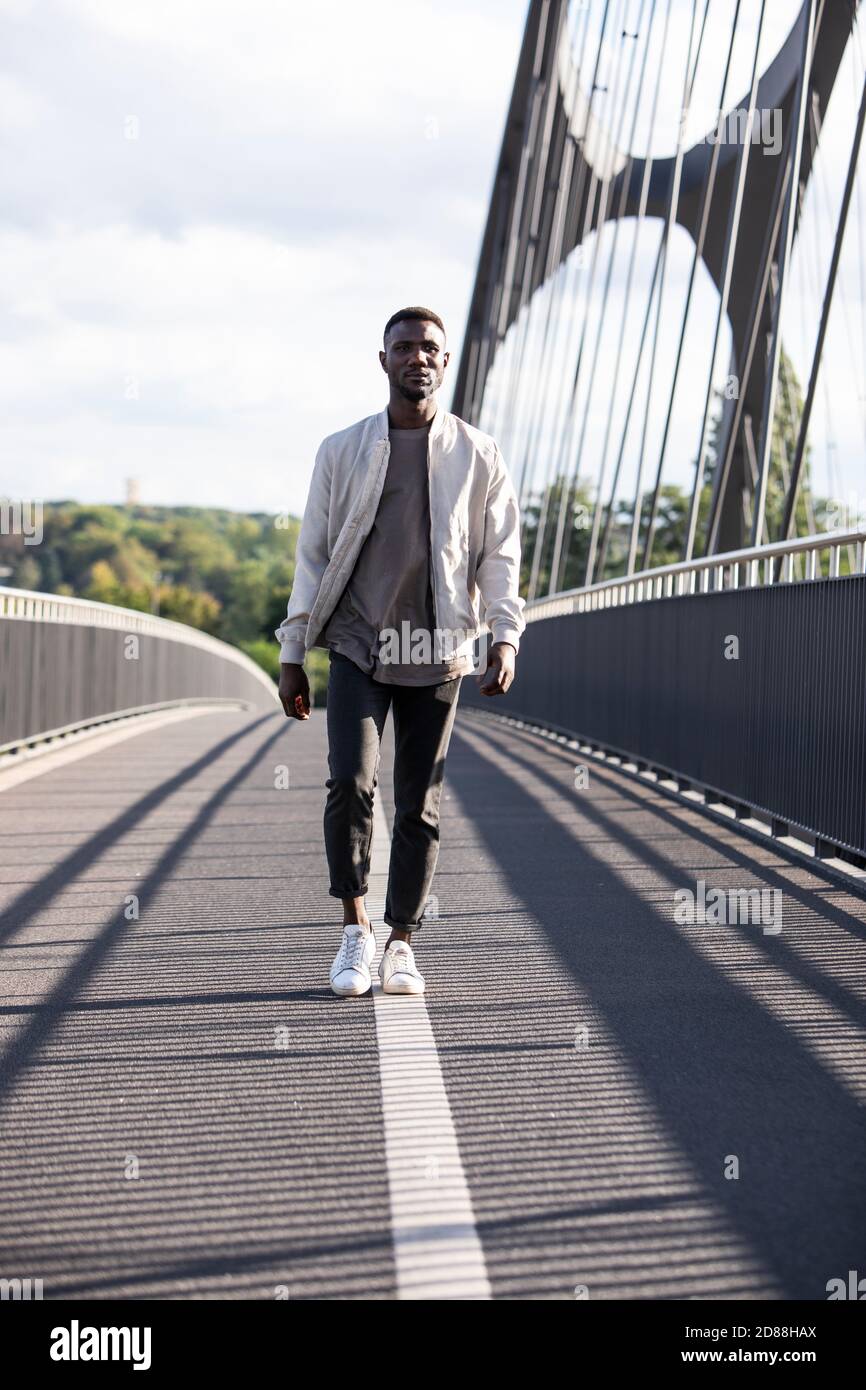 Junger Mann, der mit Zuversicht auf der Fußgängerbrücke läuft. Volle Länge. Vorderansicht. Lange Aufnahme. Stockfoto