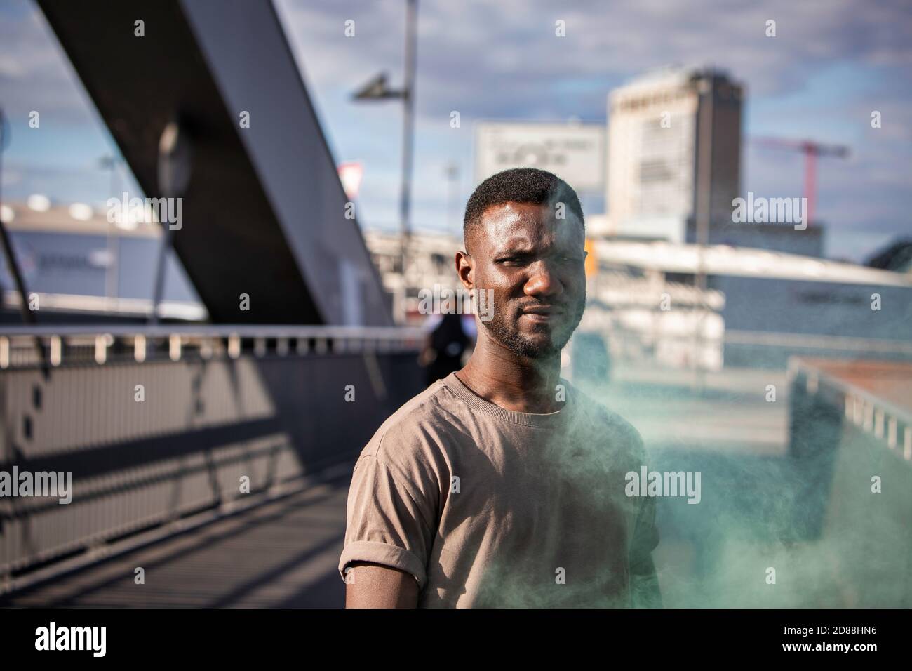 Junger schwarzer Mann, der die Kamera anschaut und grünen Rauch aufsteigt. Mittlere Aufnahme. Stockfoto